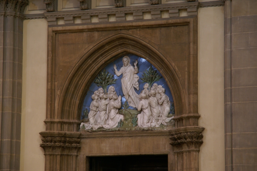 A scene of blue sky and green plants from polished plaster with white alabaster figures depicting the ascension of Christ inside brown stone archway above a door