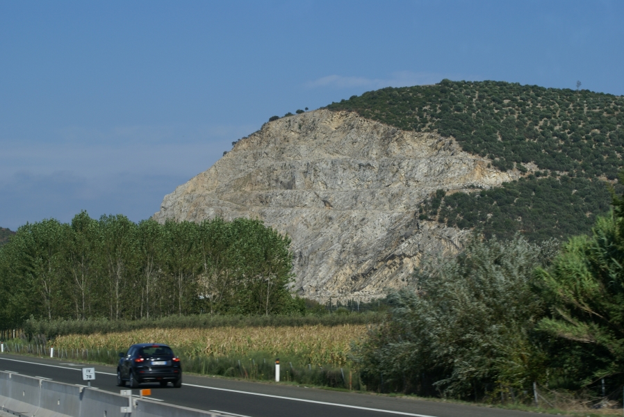 A hill with green scrub shows the scars where blocks have been cut away to reveal white stone