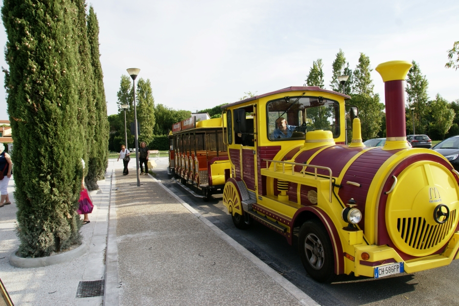 A training engine about the size of a pickup truck pulls two passenger cars all painted bright yellow and magenta