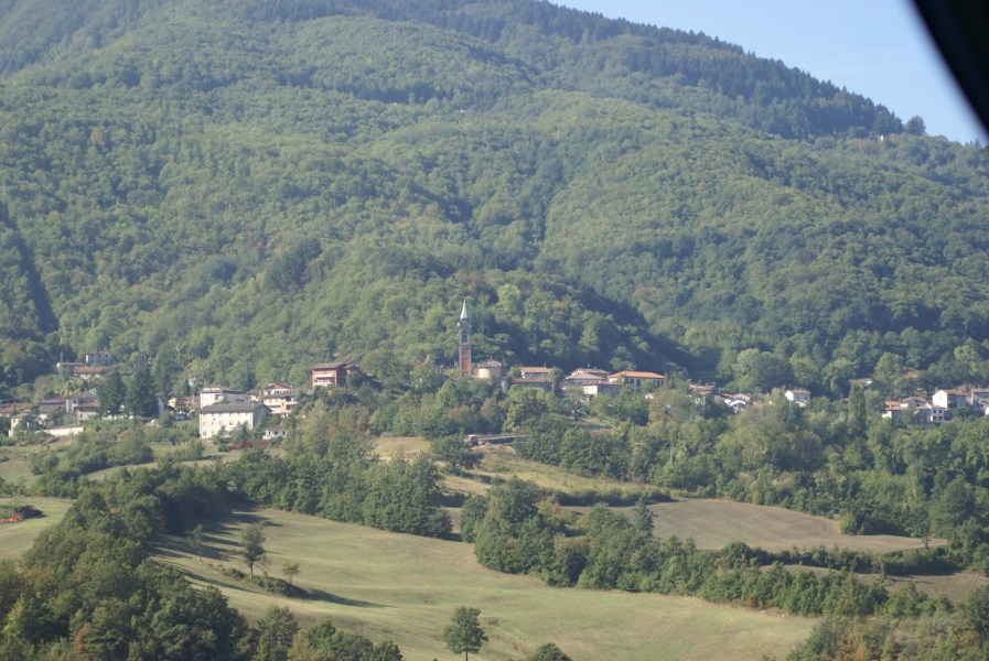 A tower sticks up above a town set against the side of a hill covered in green trees