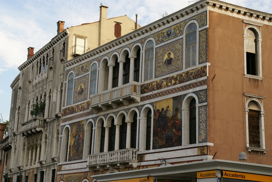 Ornate paintings of people being suited for battle adorn the lower level of a wall with vines and flowering patterns around portraits of men in historic garb above between windows and balconies of a building