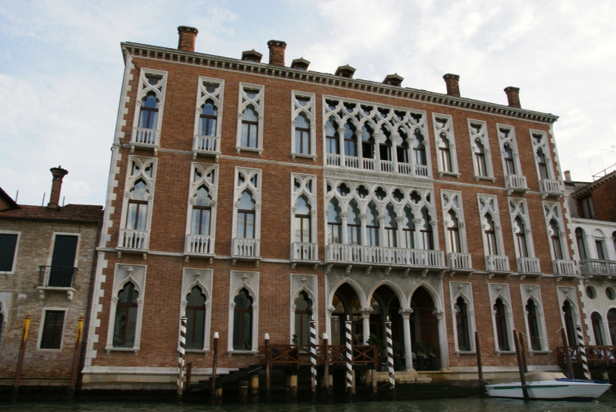 Ornate white carved stone highlights windows of a three-story red brick building with an opening on the ground floor directly to a dock in the canal