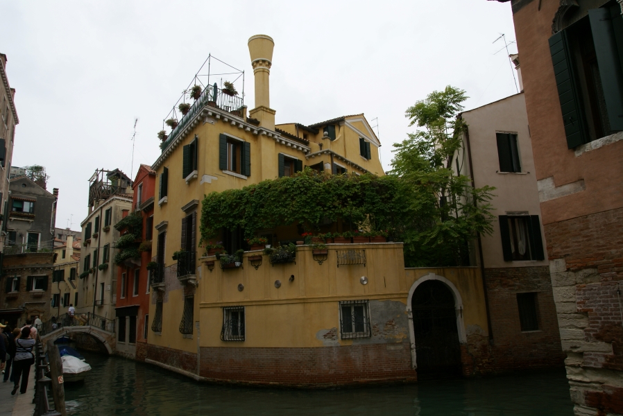 Brick walls rise from water supporting a yellow walled house and garden with a gate for a boat