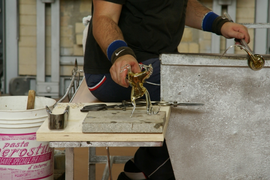 A glass worker displays a cooled sculpture of a horse reared on its hind legs he just finished shaping as a demonstration