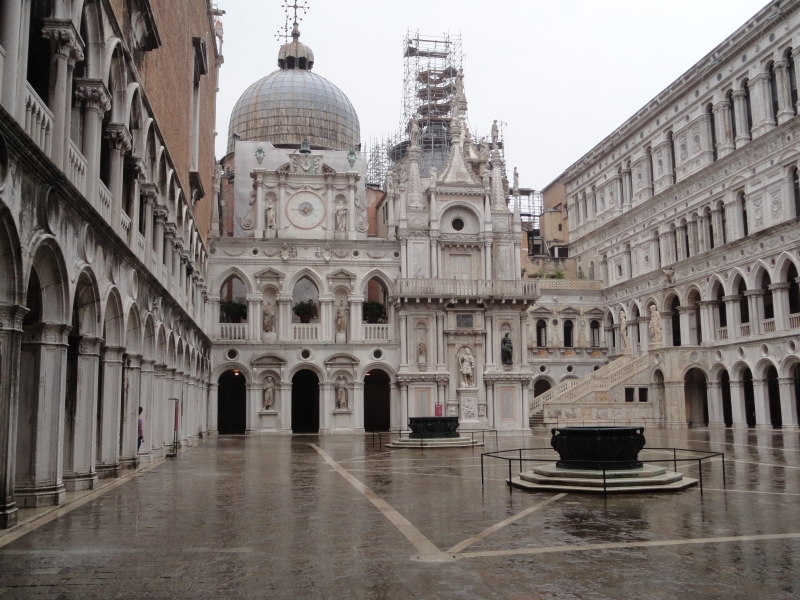 Walls with different levels of ornamentation surround a black stone courtyard wet with rain