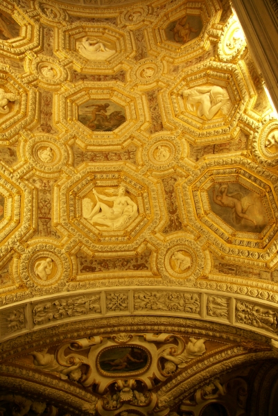 An arched ceiling with an intricately carved pattern of frames surrounding paintings and carved reliefs