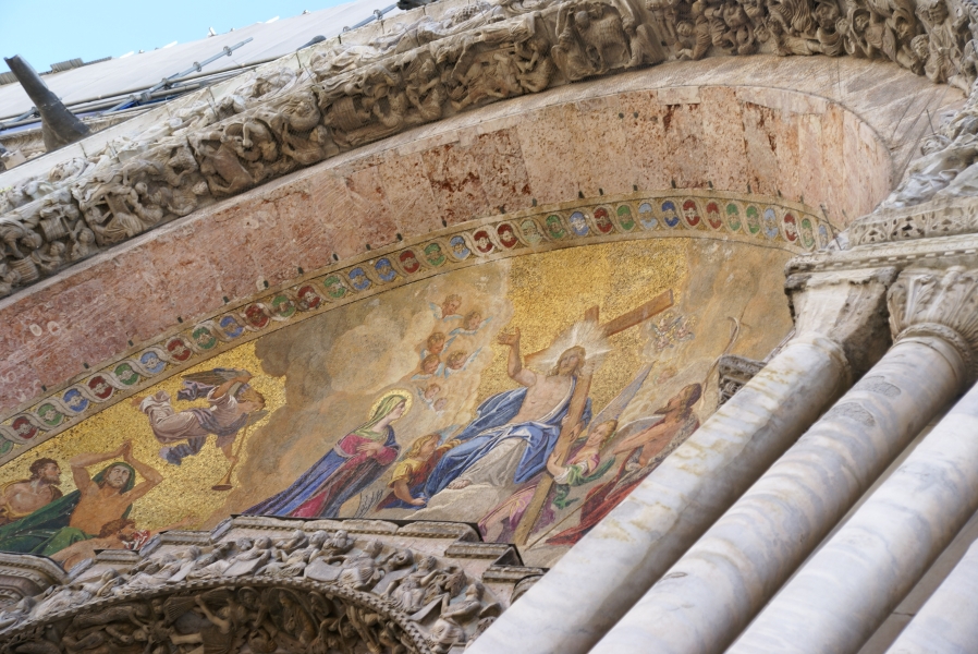 A painting with gold mosaic accents fills the arch over a door to St. Mark’s Basilica surrounded by carved stone figures
