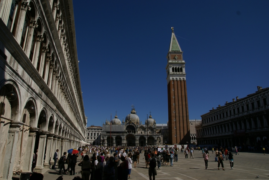 A church with several domed tops stands at the far end of a large open square with a square bell tower extending into the sky