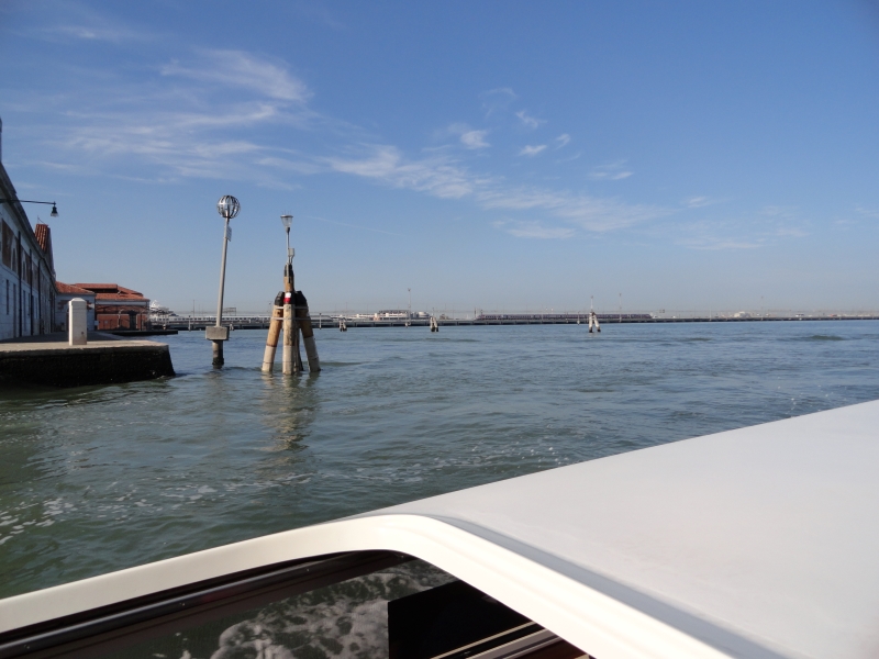 A walkway past stone buildings drops into open waters with a train on a bridge in the distance