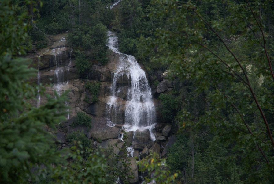 Water cascades over large boulders amongst green growth hanging on steep walls of a gorge