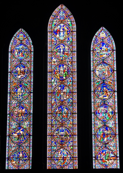 The bright sun shines through three tall narrow windows filled with colorful images made with stained-glass