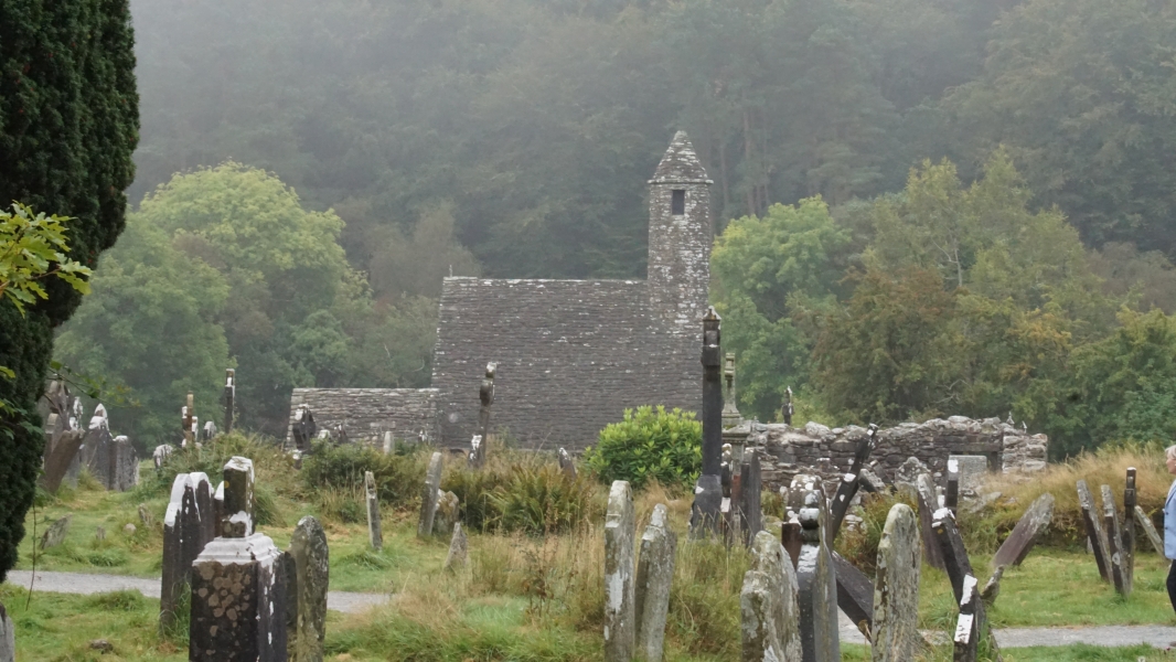 A small stone chruch with with a square tower stands amongst trees near a cemetary
