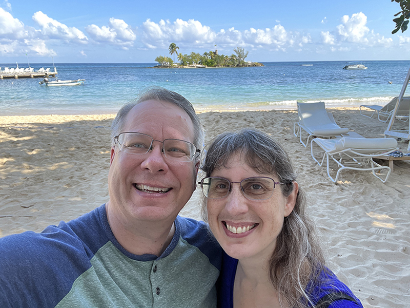 Julie and James on a beach with blue waters and a small island in the distance