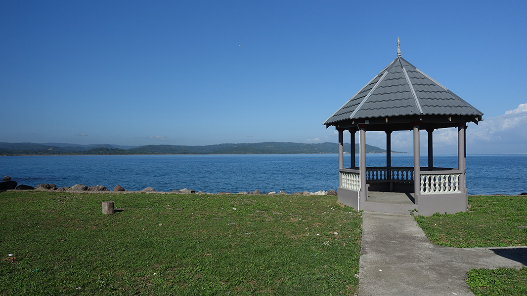 A gazebo stands in grass with the ocean spreading out beyond