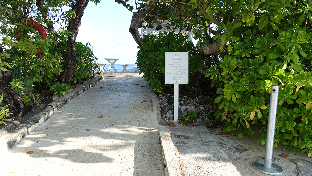 A sign next to an opening in the trees tells visitors cloths are not allowed when on the island