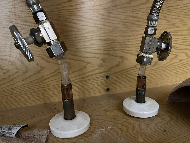 Two copper pipes stuck up in a cabinet with ice coming out of the top holding plumbing valves in the air