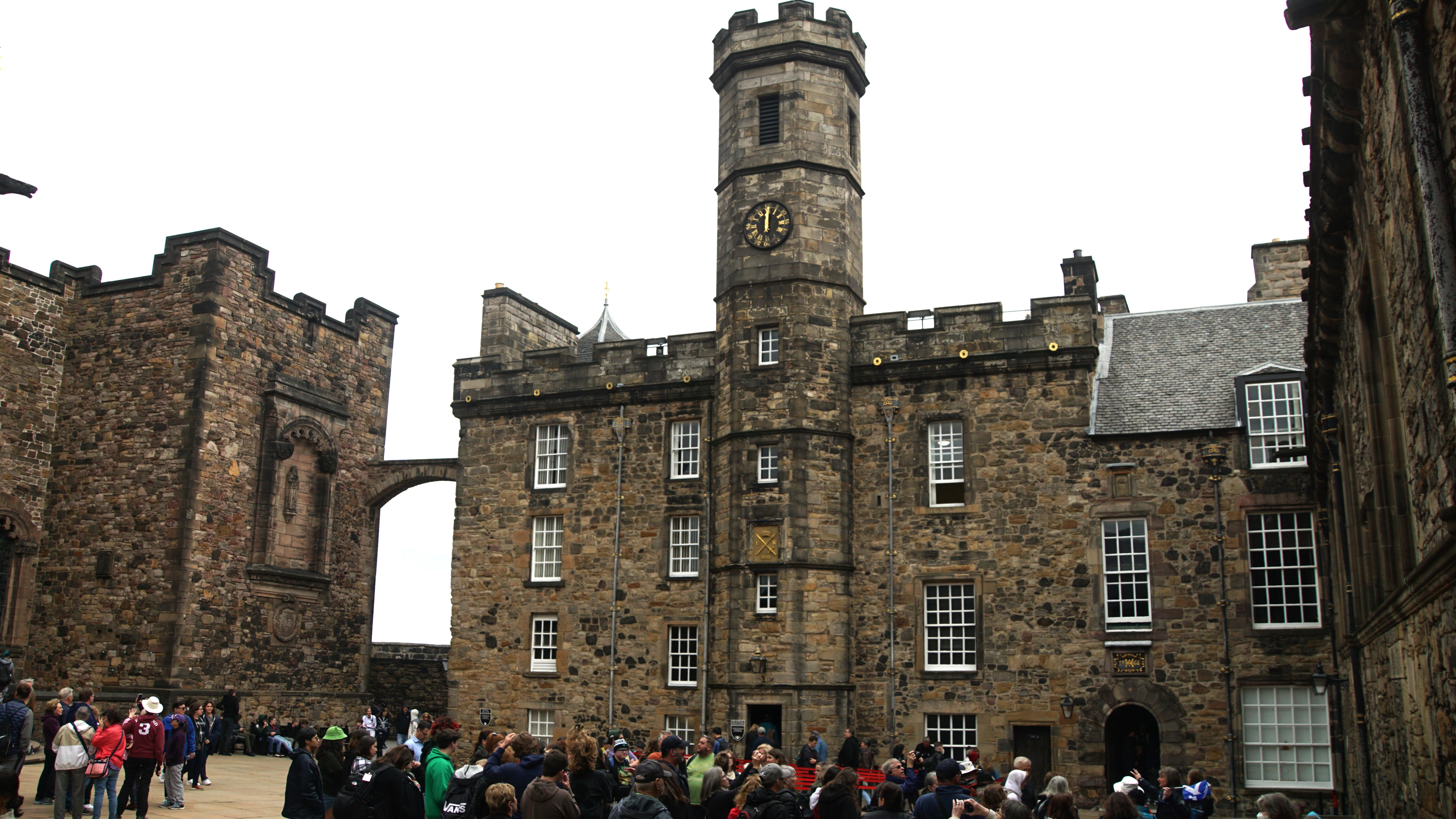 Crowd in courtyard by 3 store stone structure with clock tower