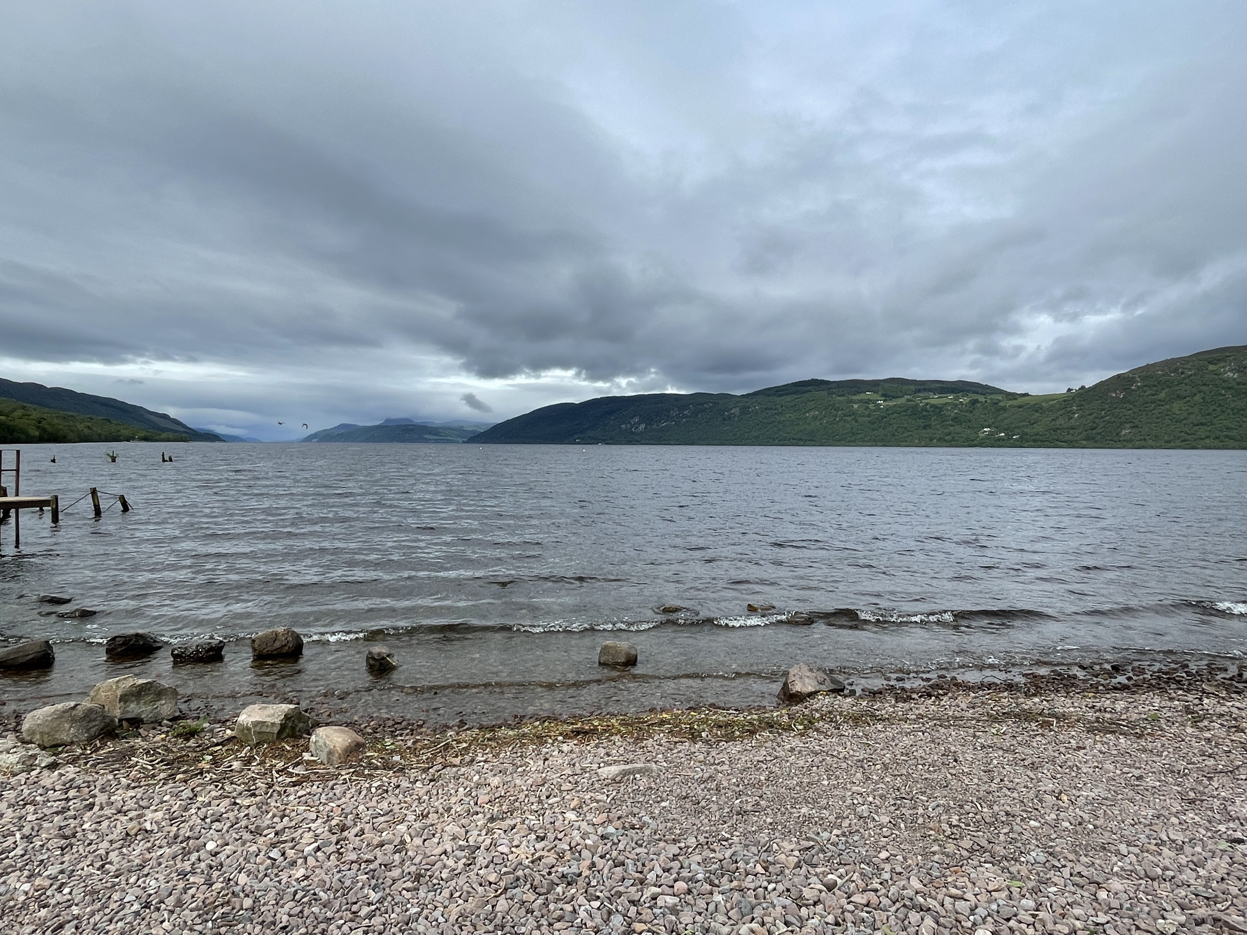 Gravel stone beach at a lake with green hilss and gray clouds
