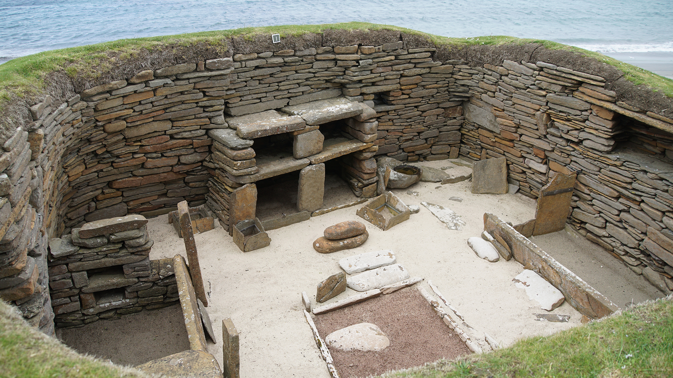 Stone walls and furniture inset in green hillside with ocean in distance