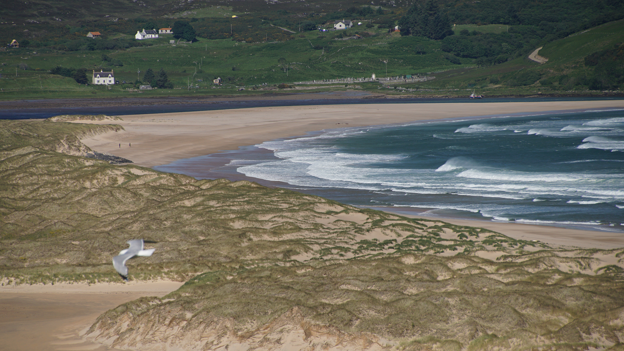 Waves crashing on a brown sand beach below green hills