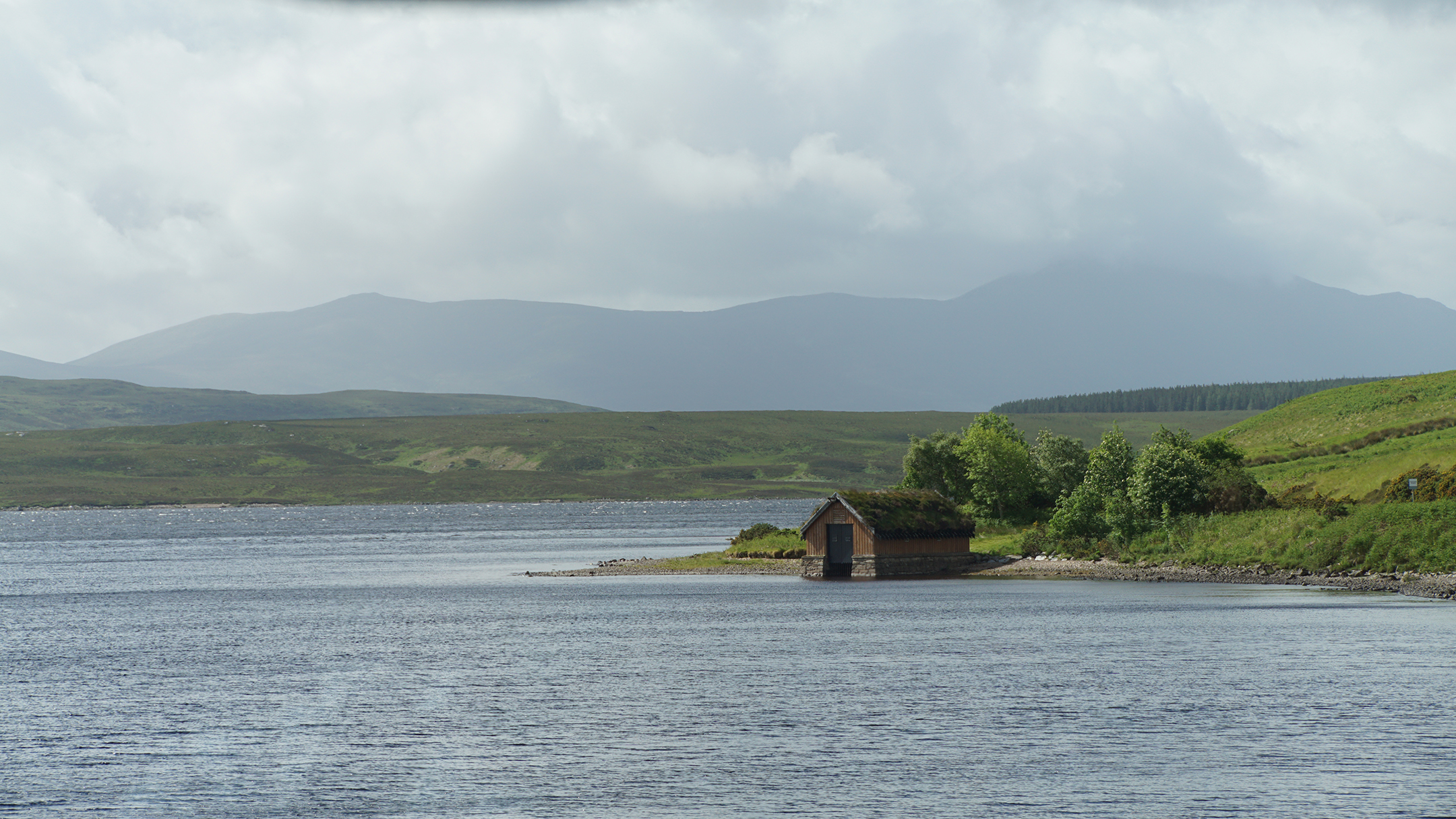 A boathouse on a calm lake surrounded by green hills
