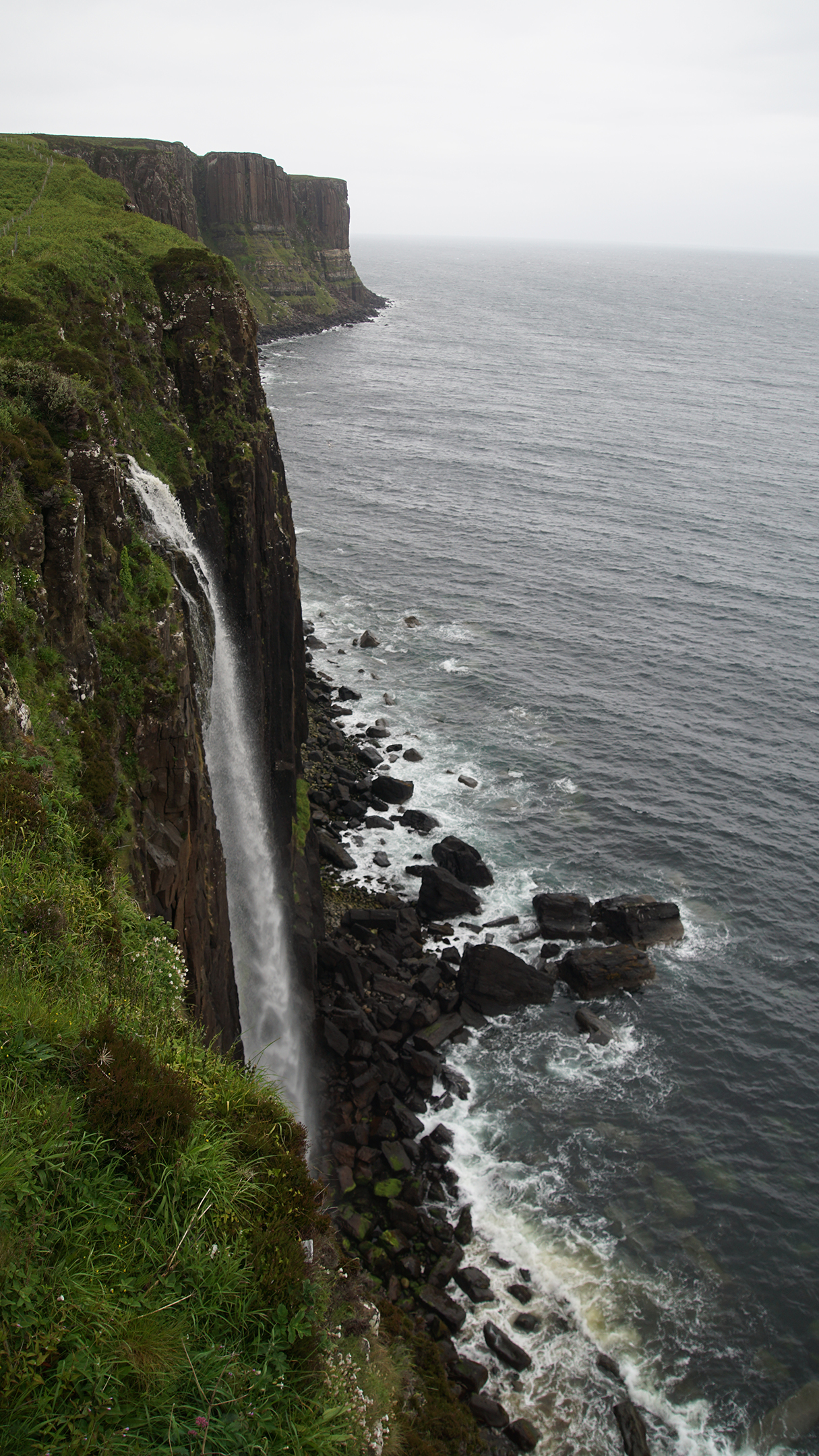 A waterall empties over a stone cliff into the ocean