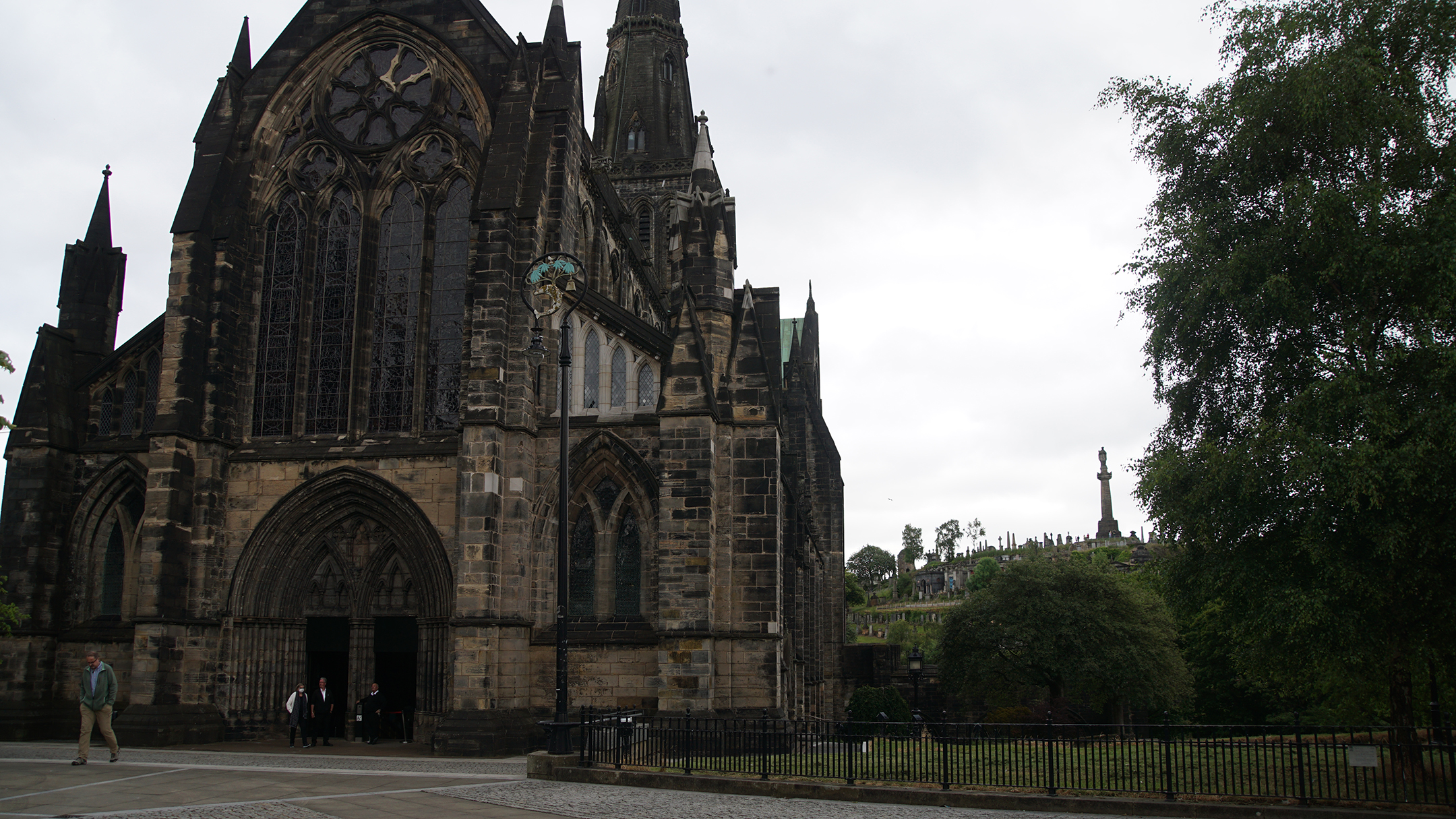 Stone church next to green park with a hill of stone crypts in the distance