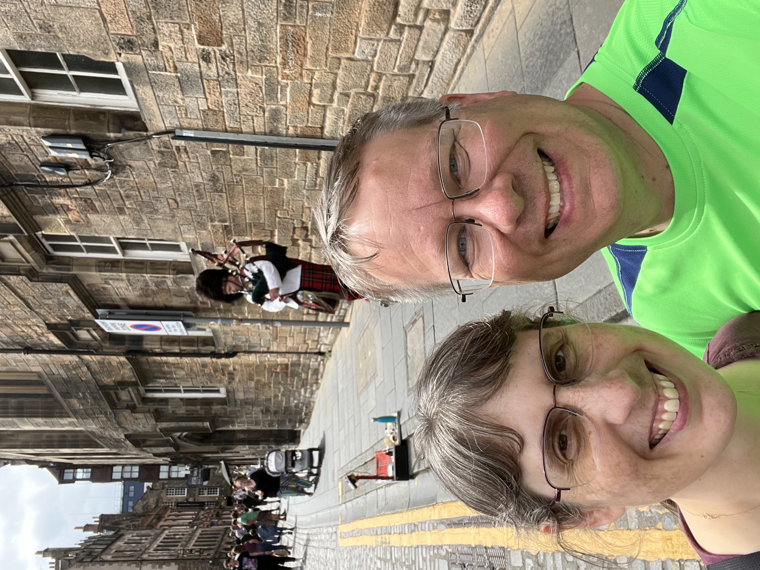 James and Julie in front of an old stone building with a bagpiper playing