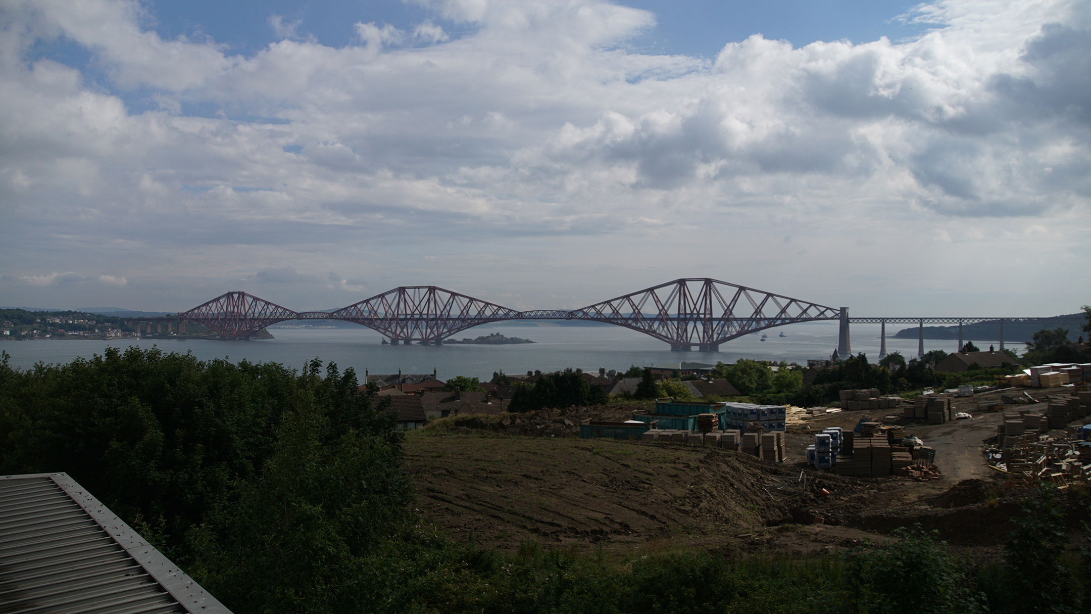 A bridge of red steel and three spans crosses a river