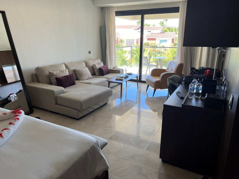 A couch, coffee table, and chair sit in front of a sliding door to a balcony with a small table and two chairs