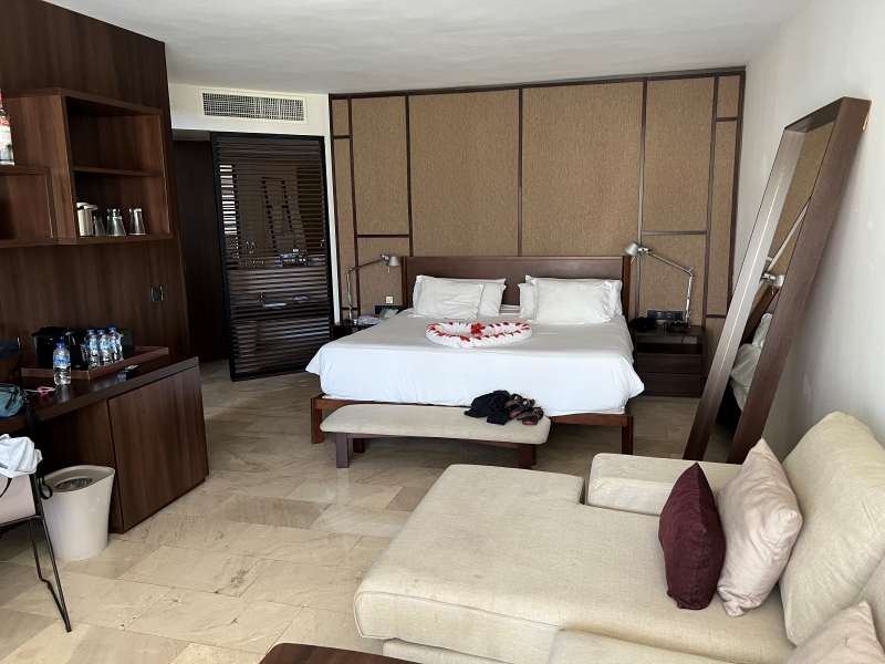 A bed sets against a wall with slats to the left with a bathroom sink visible beyond