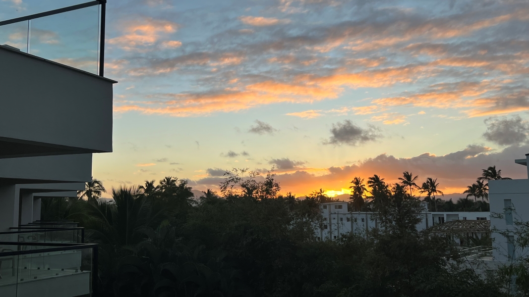 Yellow colors light the clouds as the sun sets behind mountains in the distance