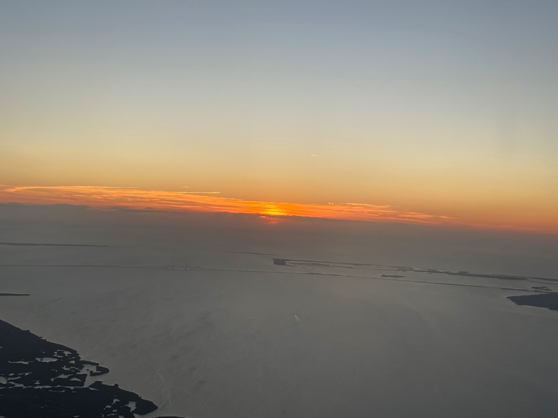 The sun sets over water as seen from the window of a plane as it starts the landing process in Tampa