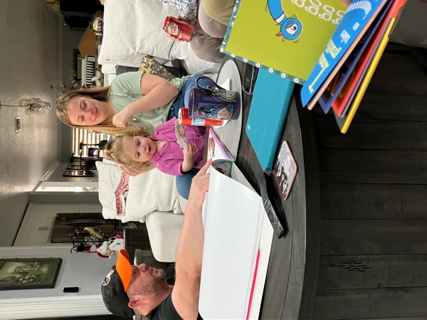 A young girl with a pink shirt blonde curly hair plays with stickers with her mom at a messy coffee table