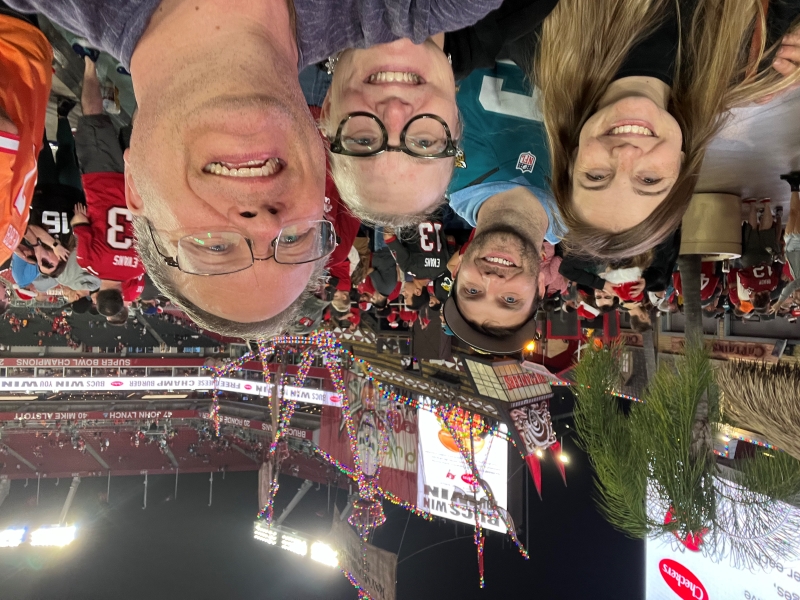 Four people pose for a selfie with a pirate ship covered in Christmas lights in a stadium in the background