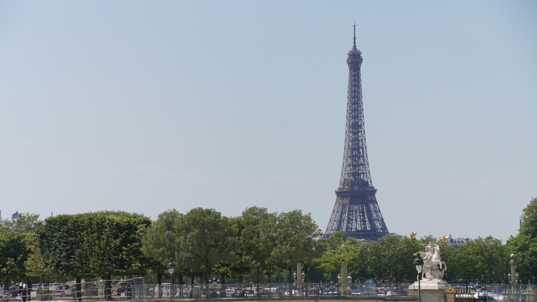The Eiffel Tower stands above green trees and a statue