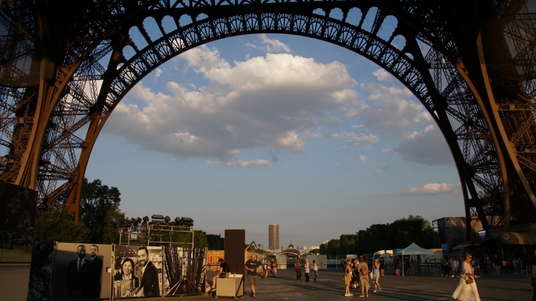 The brown iron arch at the base of the Eiffel Tower frame clouds beyond