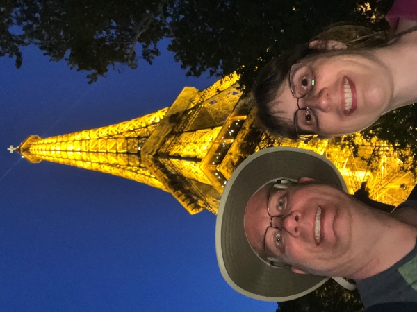 Julie and James with the Eiffel Tower lit with yellow-orange lights