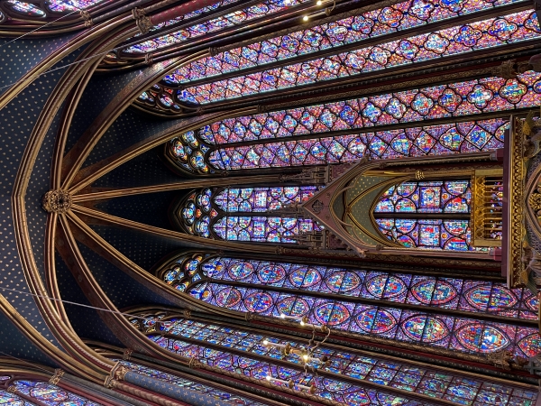 Stained glass windows tower on both sides and around the curved end of a gothic stone interior