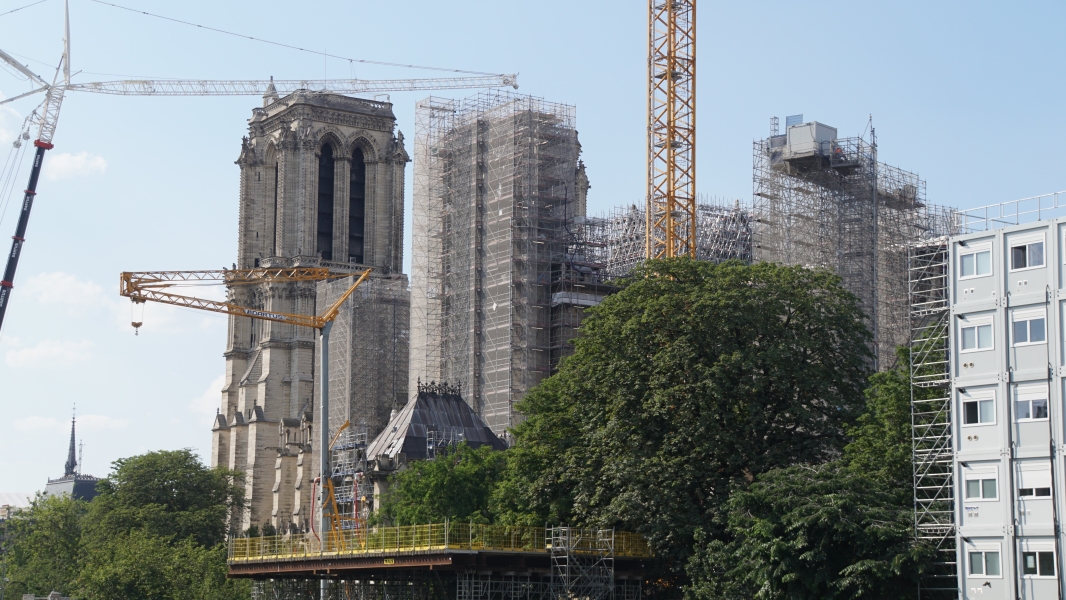 Scaffolding hides the end of a stone cathedral with several cranes and a multi-story temporary office building