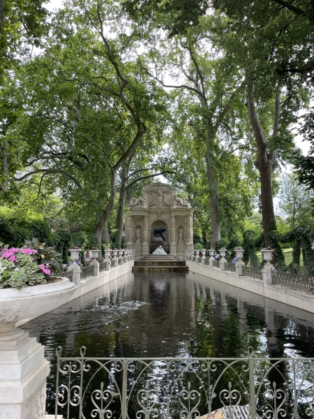 A long narrow reflecting pool below trees ends in a tan stone fountain with Italian sculptural detailing