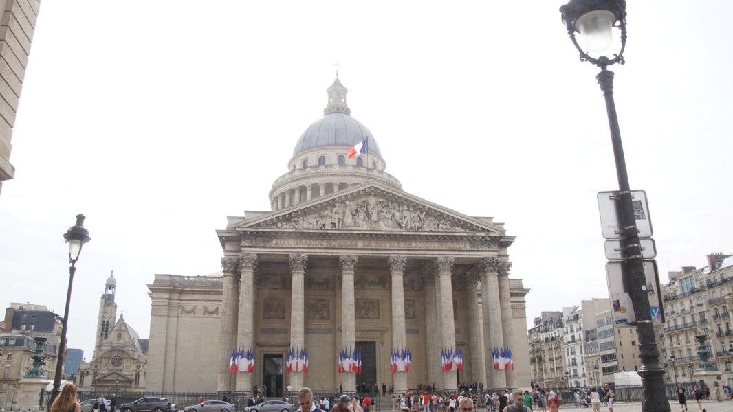 A towering dome above a massive building with Grecian entry extends above the neighboring six-story buildings