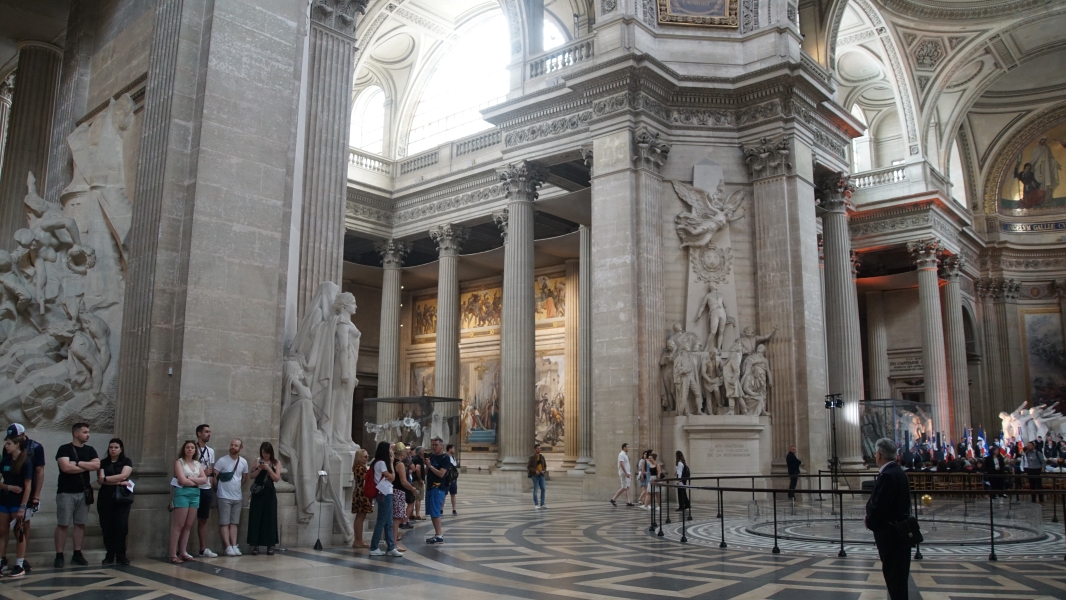 Massive white stone sculptures adorn the walls inside a church like building with ornate tile floor patterns