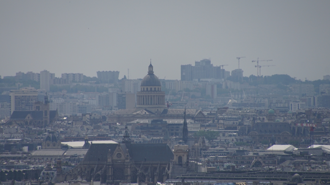 A domed building visible towering above neighboring buildings as seen from a distance on a hazy day