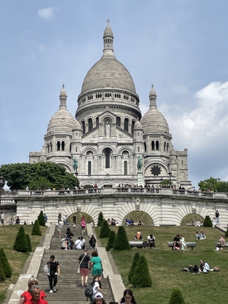 A white stone building with one large and several smaller domes sits above stairs and landings amongst green grass