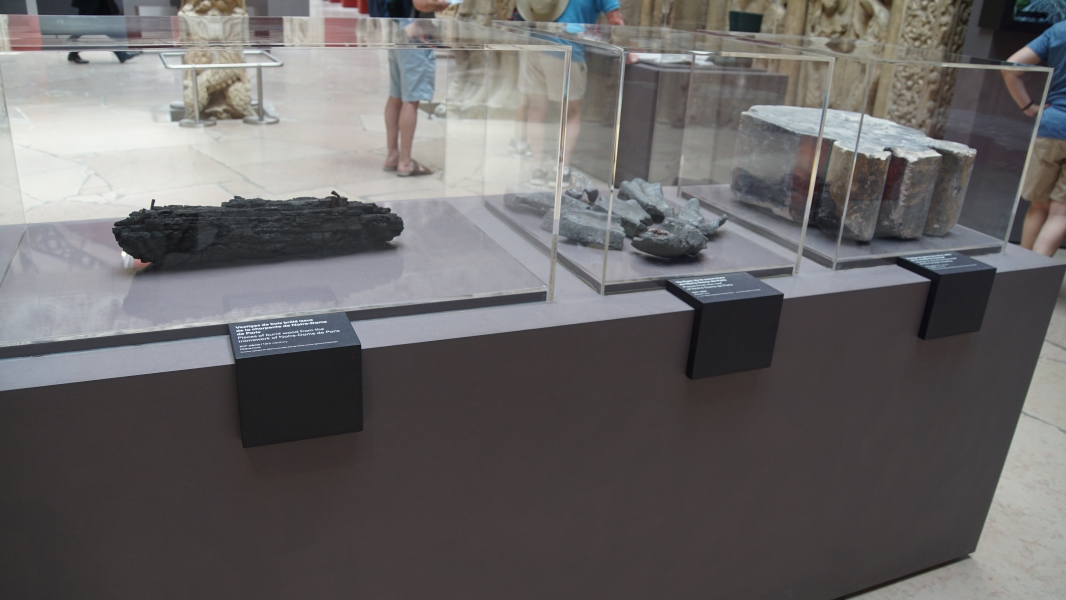 A charred piece of wood, melted lumps of lead, and a damaged piece of carved stone on display inside protective cases