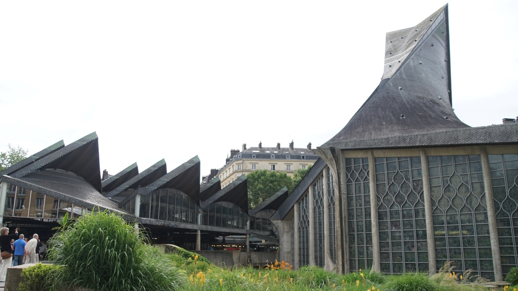 A slate covered sloped roof extends above stained-glass windows neighbored by a series of smaller glass and slate roof shade structures