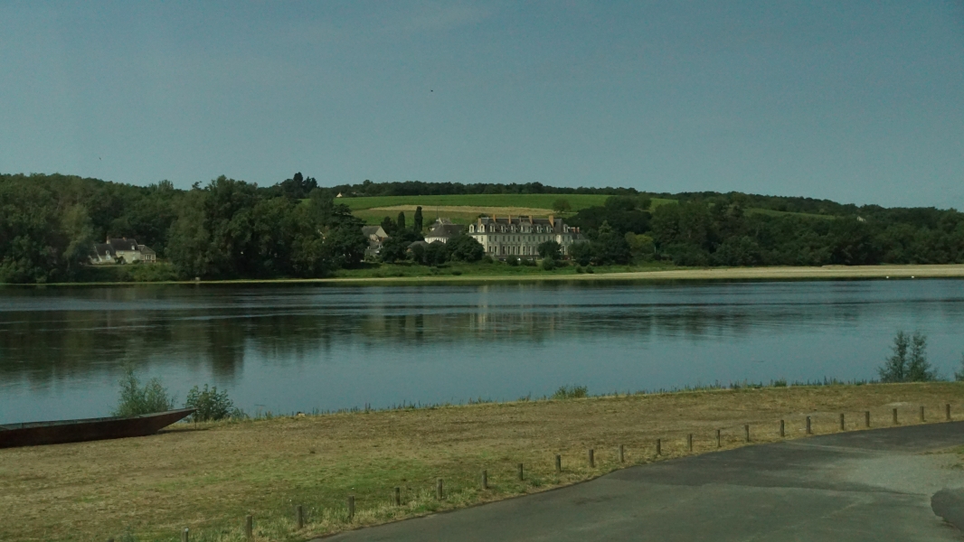 A large building with white stone walls and slate mansard roof stands between fields and a river