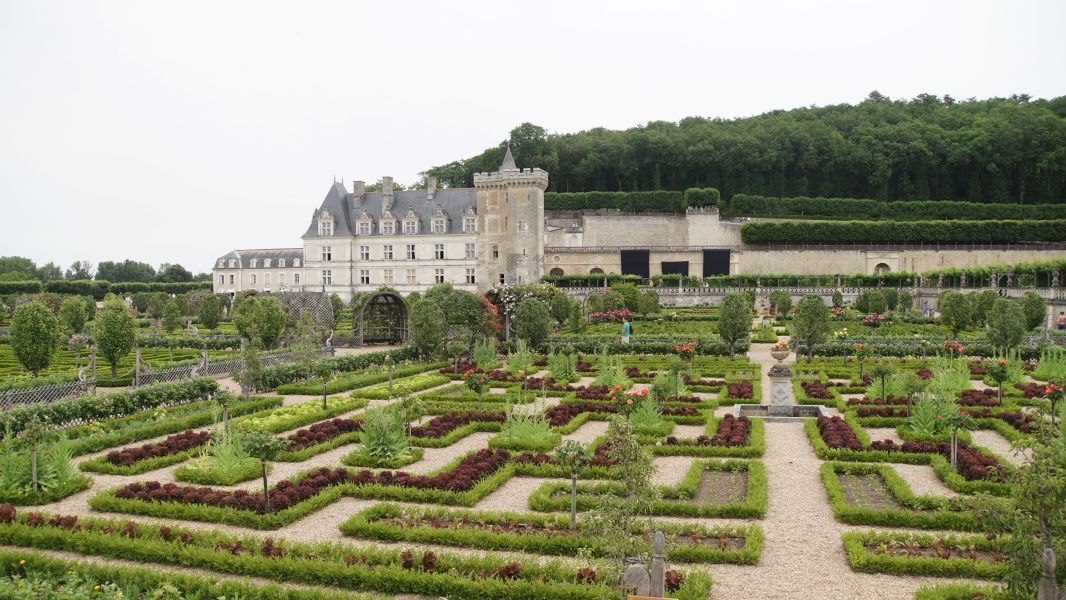 Formal patterned gardens with vegetables in front of a large white stone chateau
