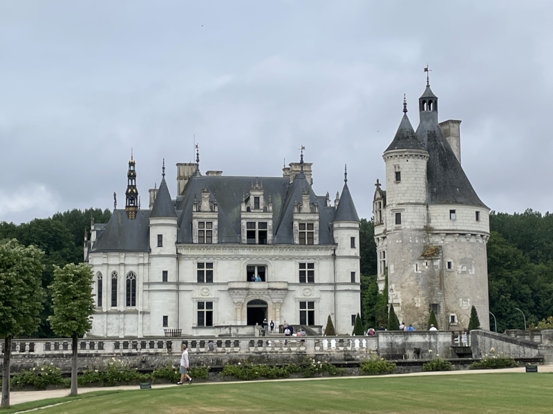 IA gothic stone tower stands separate from a stone three-story chateau with white walls and steep slate roof